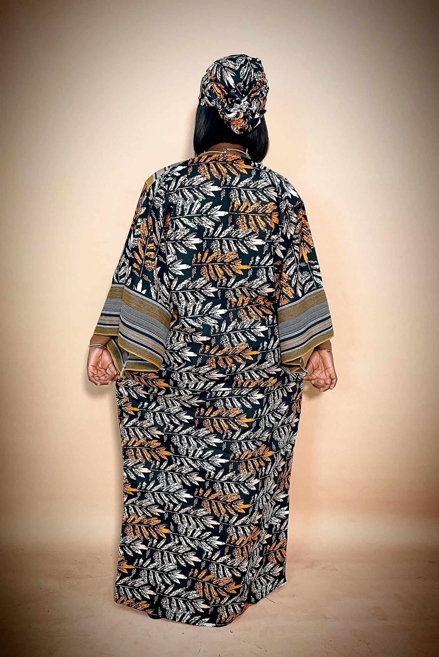Back view of Woman wearing a long, patterned African ankara dress with a matching headscarf on a beige background