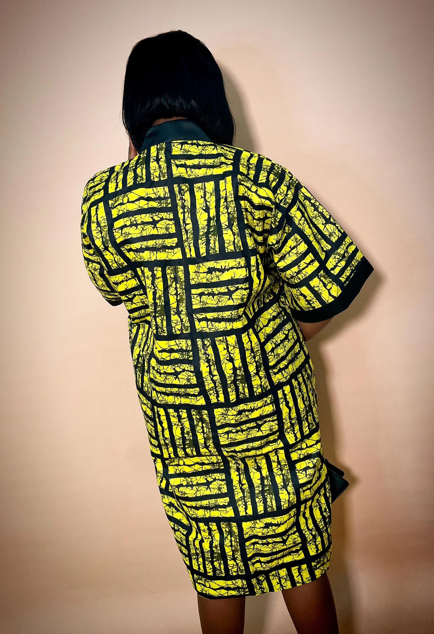 Back view of a person wearing a bright pink african print ankara dress with black trim on a beige background
