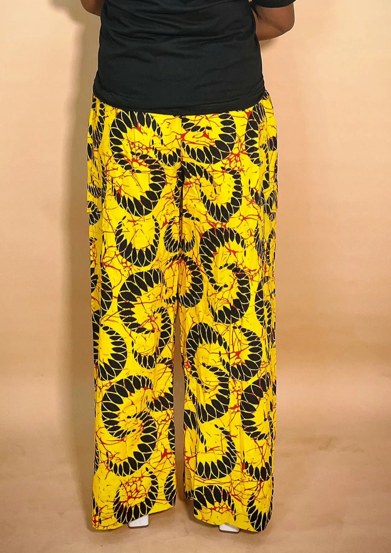 Front view of a yellow patterned Ankara baggy pant with gold chain detail on a blurred background