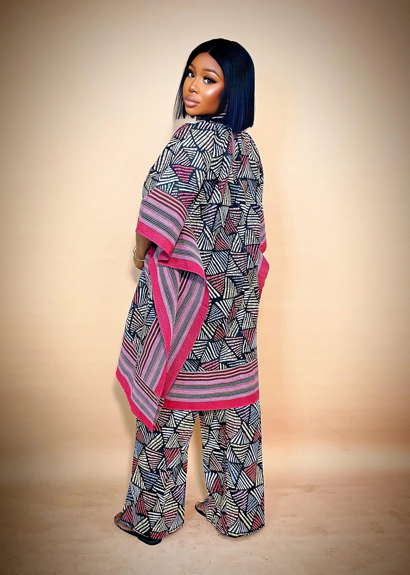Person wearing a patterned outfit with a large scarf against a beige background