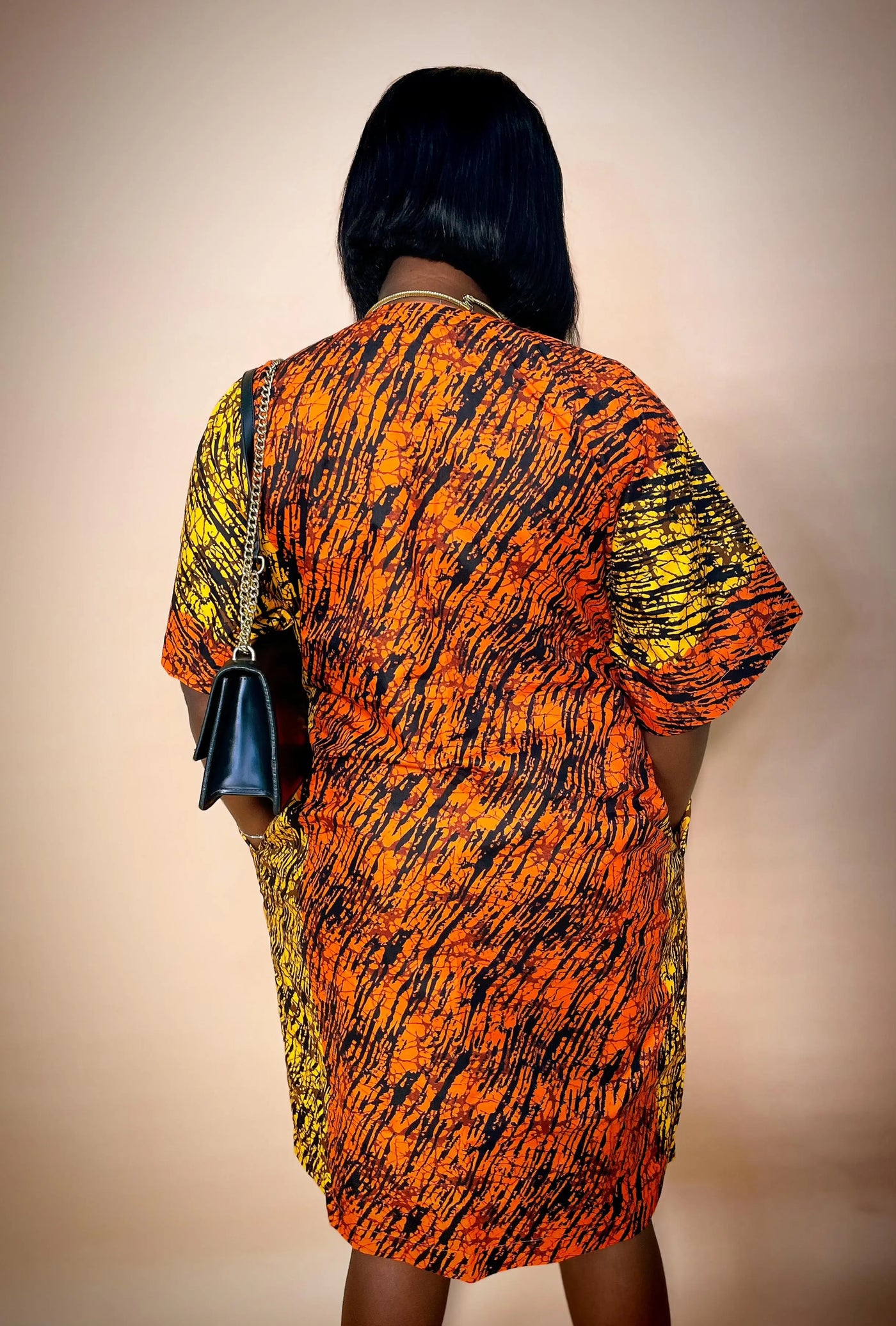 Person wearing an orange and yellow patterned dress with a plain background