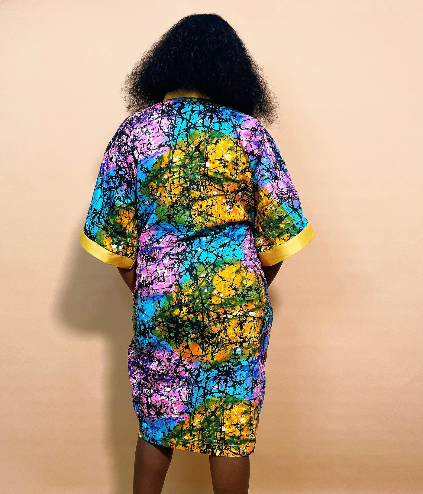 Back view of a woman wearing an African Multicolored Short Bubu Gown against a brown background
