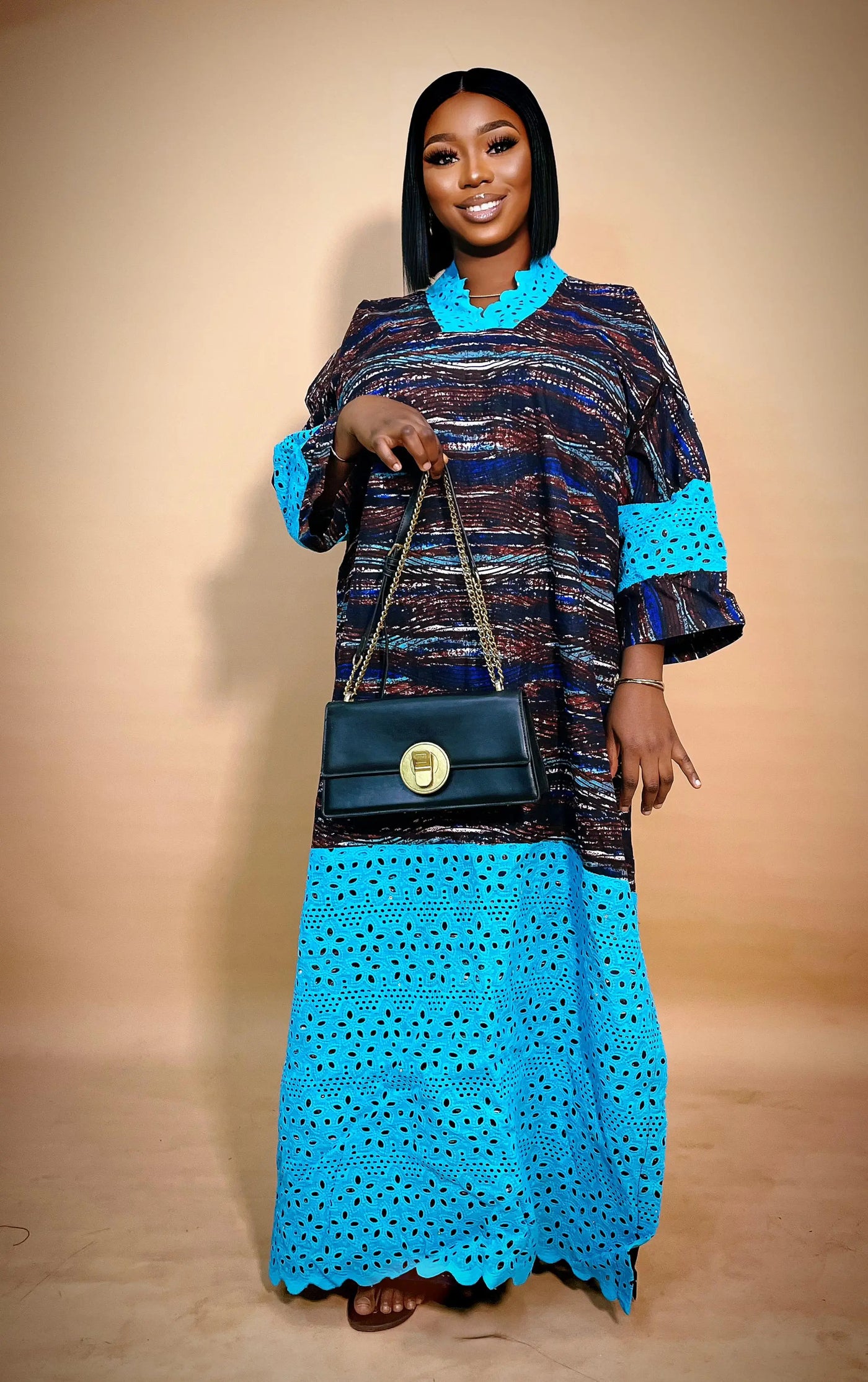 Woman wearing a blue and patterned outfit holding a black handbag against a beige background