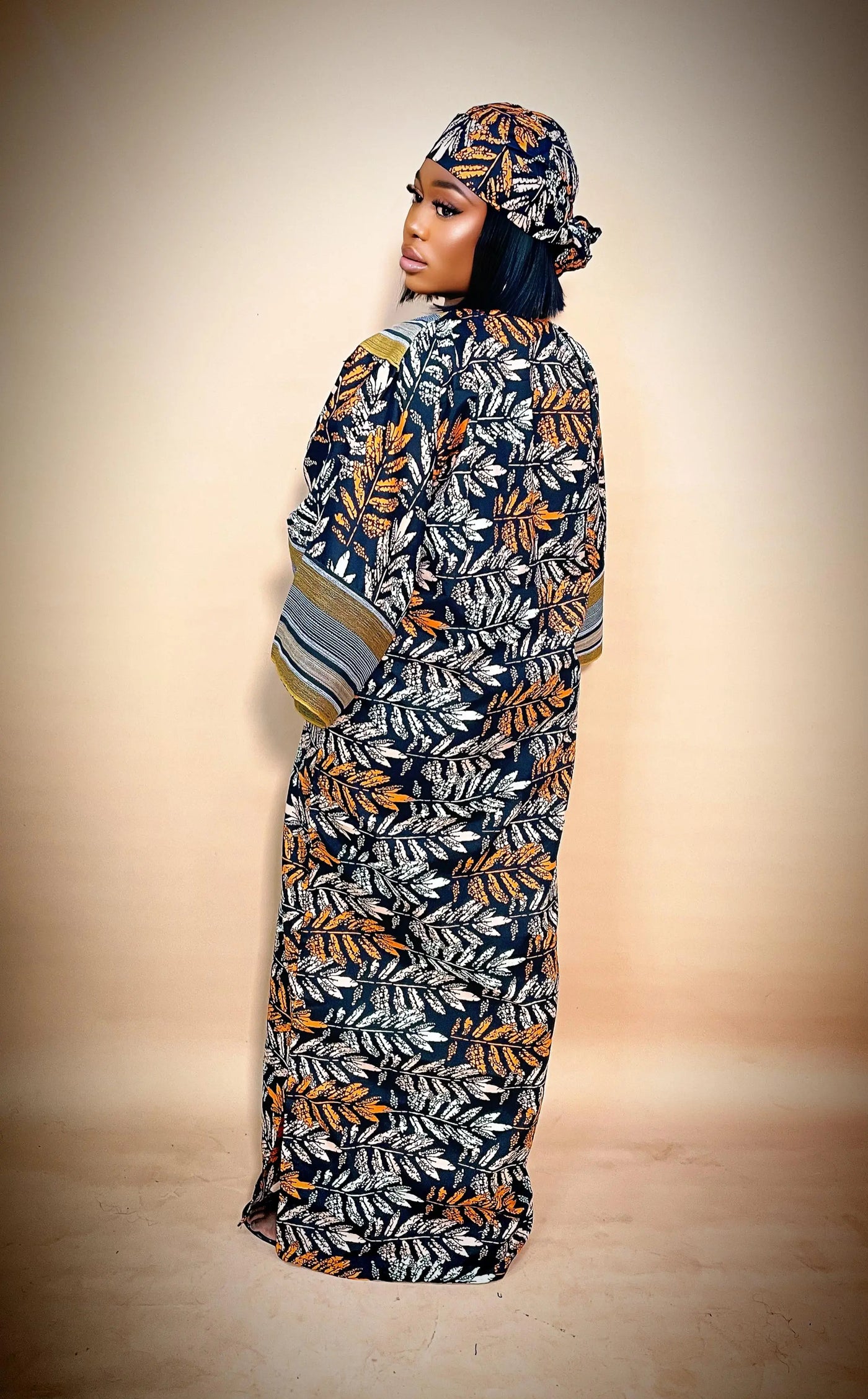 Woman wearing a long, patterned African ankara dress with a matching headscarf on a beige background