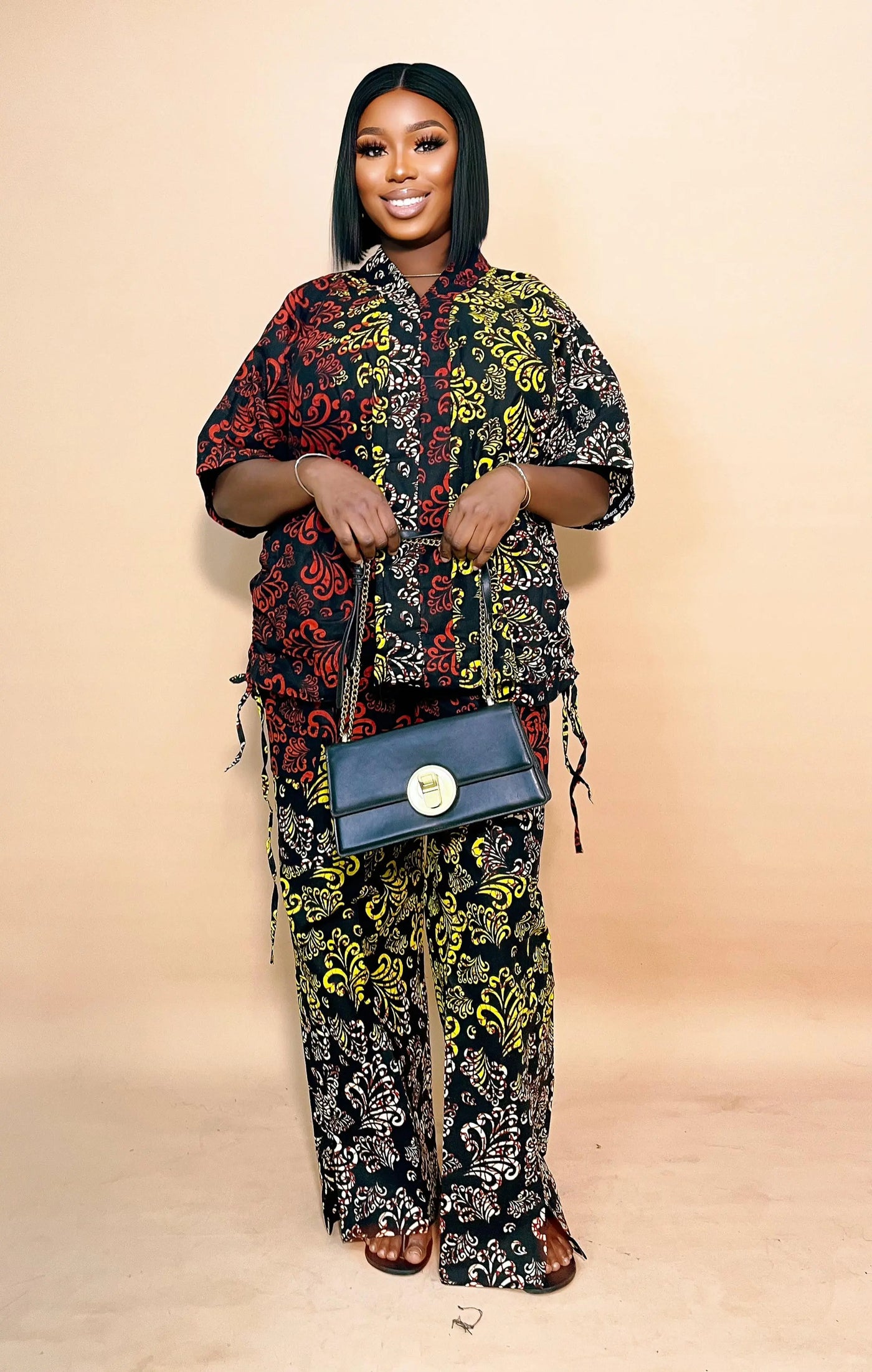Woman wearing a patterned African Two Piece Set with a blue handbag on a beige background