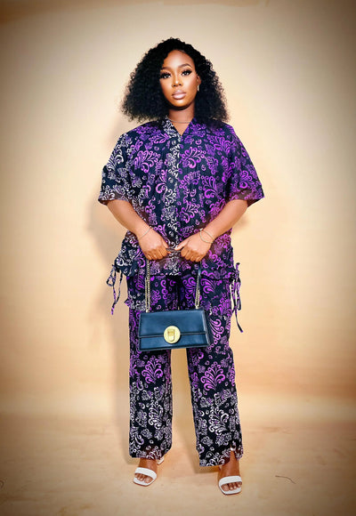 Woman wearing a purple and black African Two Piece Set against a beige background holding a blue handbag against a beige background